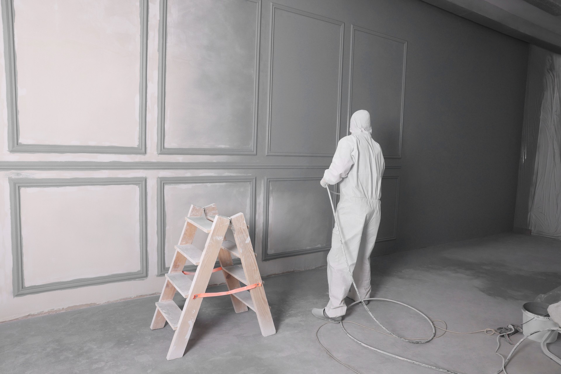 Decorator dyeing wall in grey color with spray paint indoors, back view